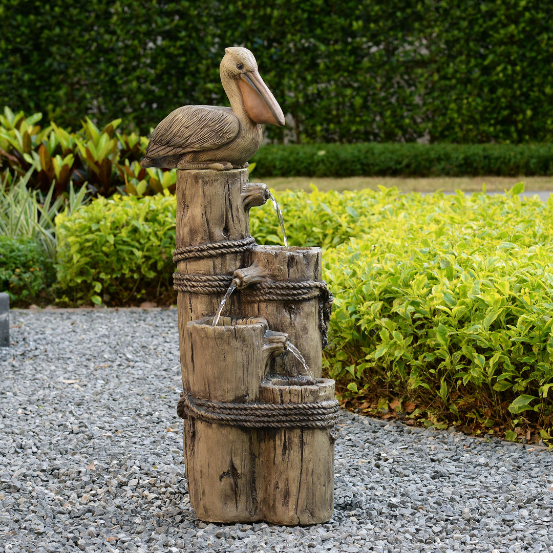 a pelican sits on the top of a wooden post water fountain in the driveway of a beach houses