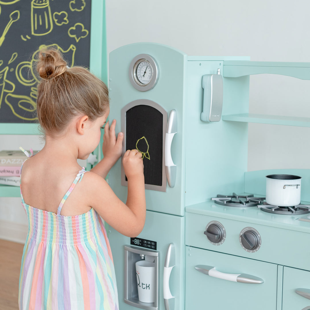 A young child drawing on a chalkboard of a Teamson Kids Little Chef Westchester Retro Kids Kitchen Playset, Mint.