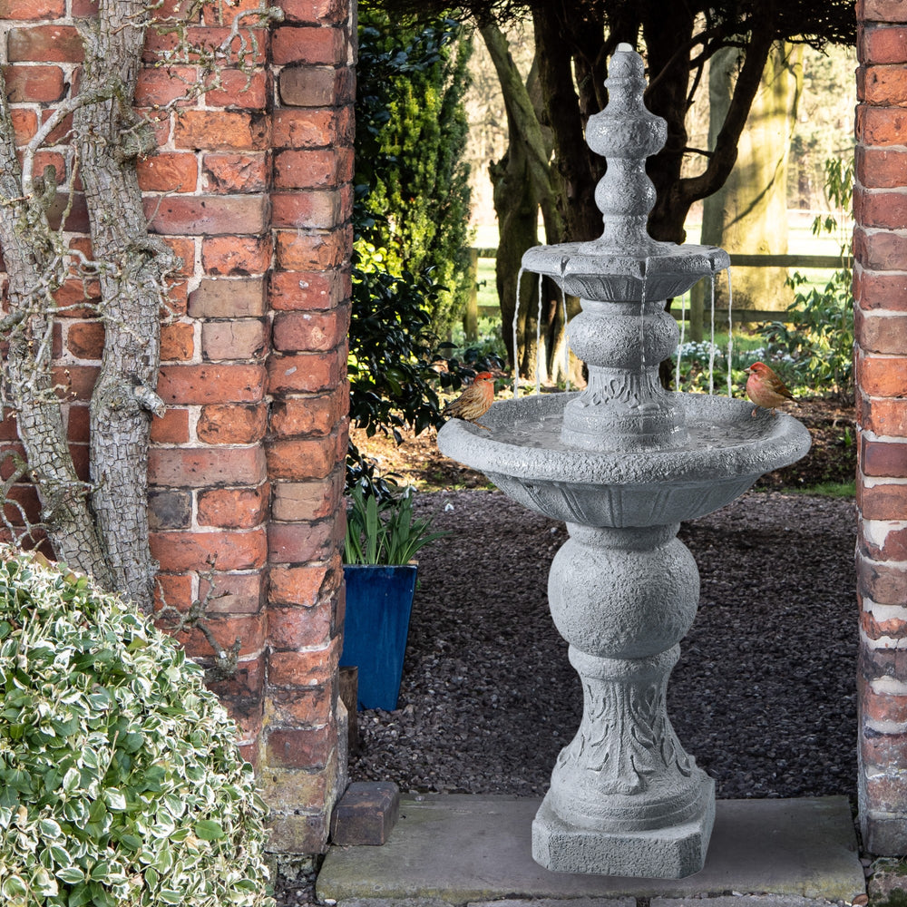 A two-tier faux gray stone birdbath water fountain in a garden