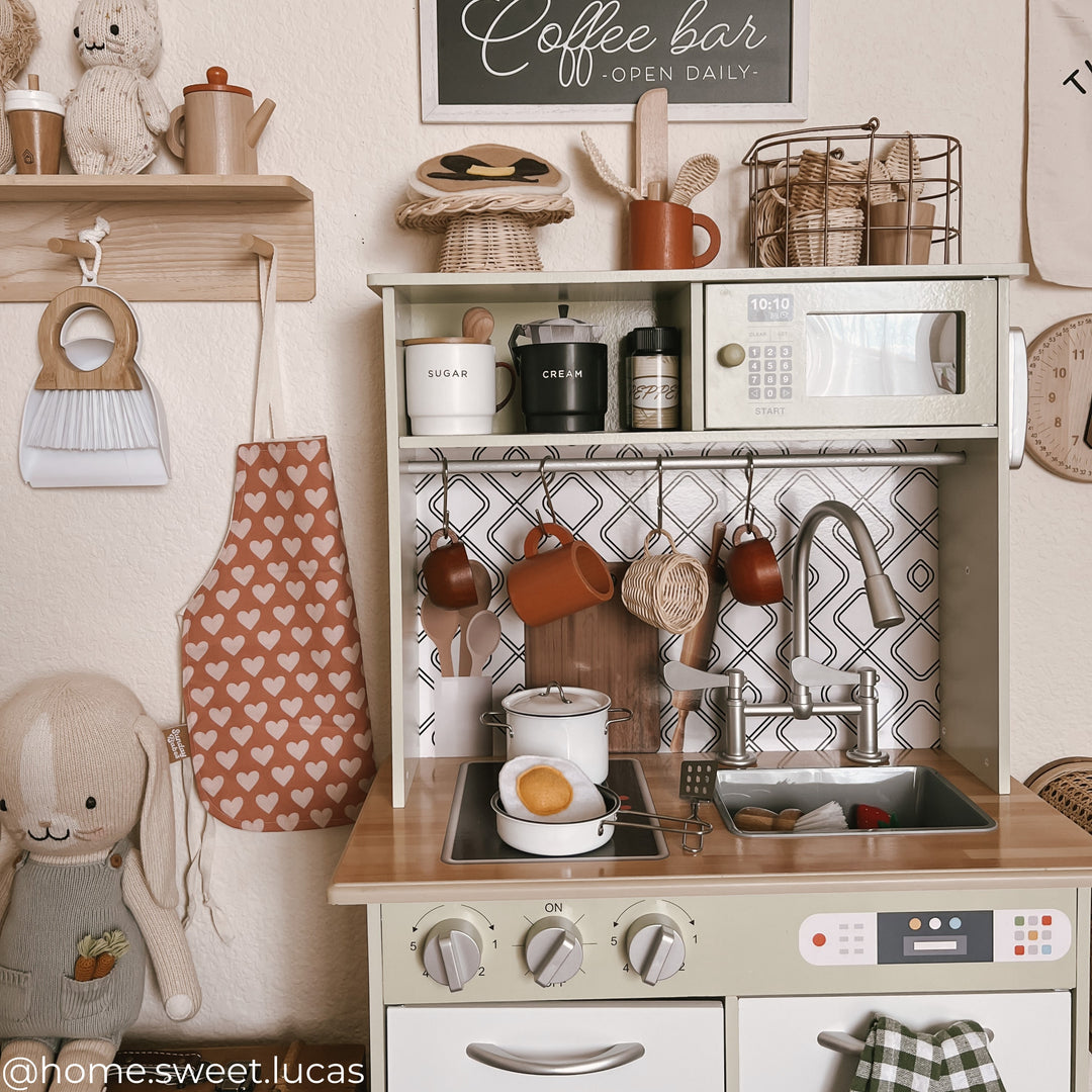 Influencer image of the small kitchen in a child's neutral colored playroom, complete with kitchen props.