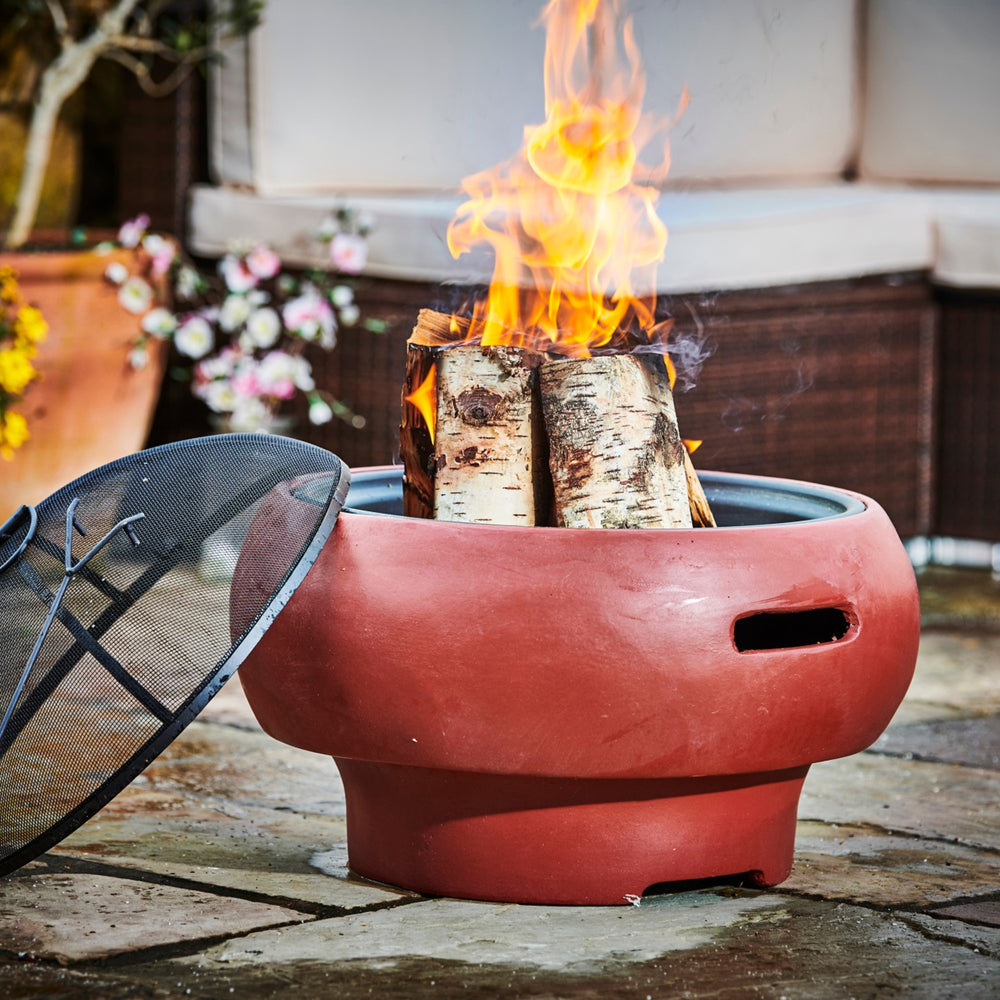 A round red wood burning fire pit with a spark screen