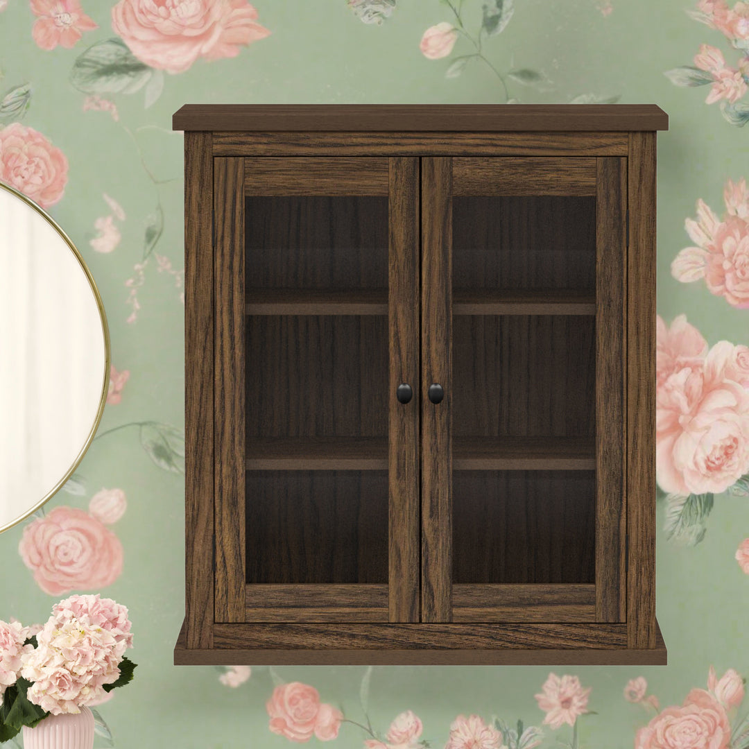 A two-door walnut finished wall cabinet hung on a green and pink floral wall.