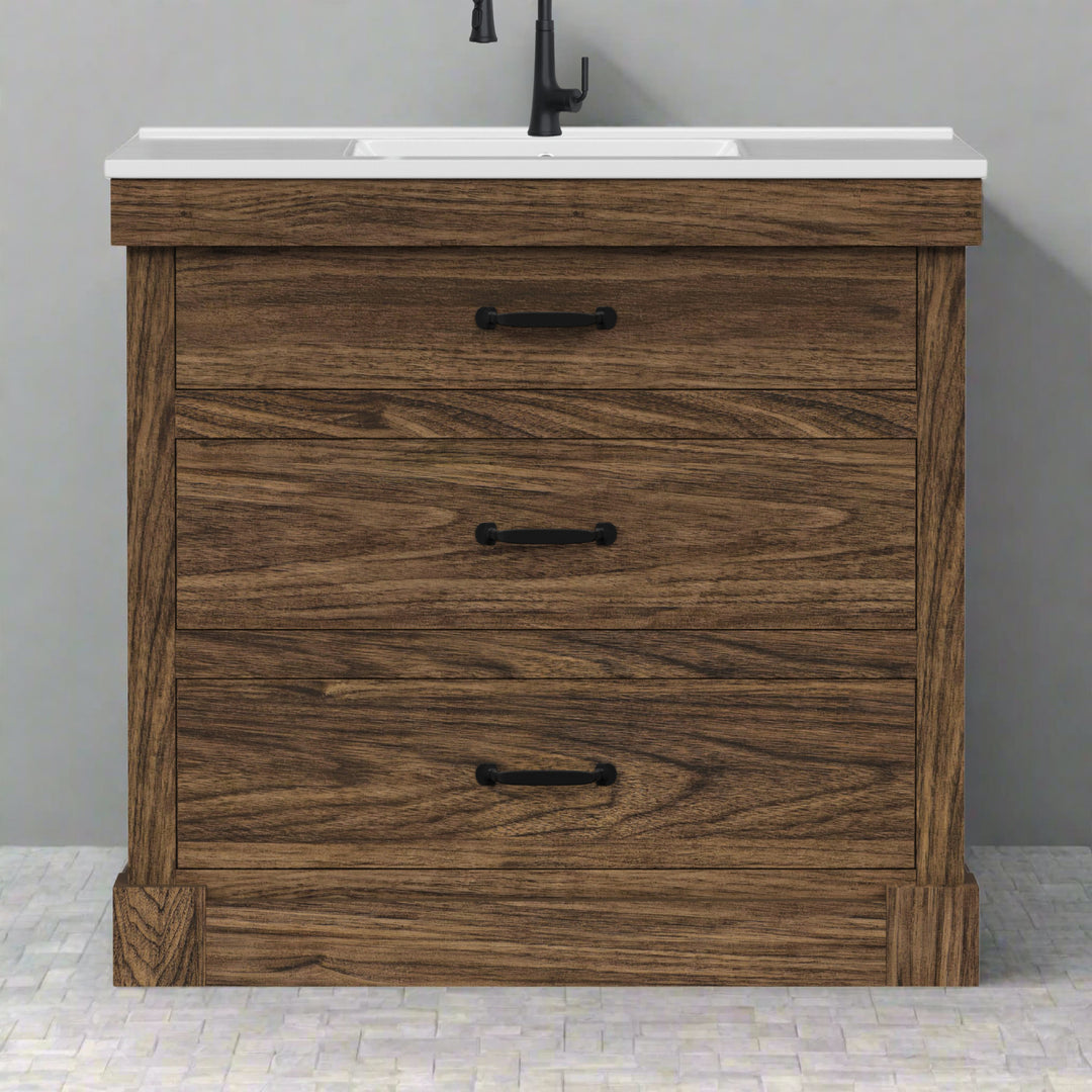 Walnut finished sink vanity with black hardware and white ceramic countertop against a gray wall on tiled floor.